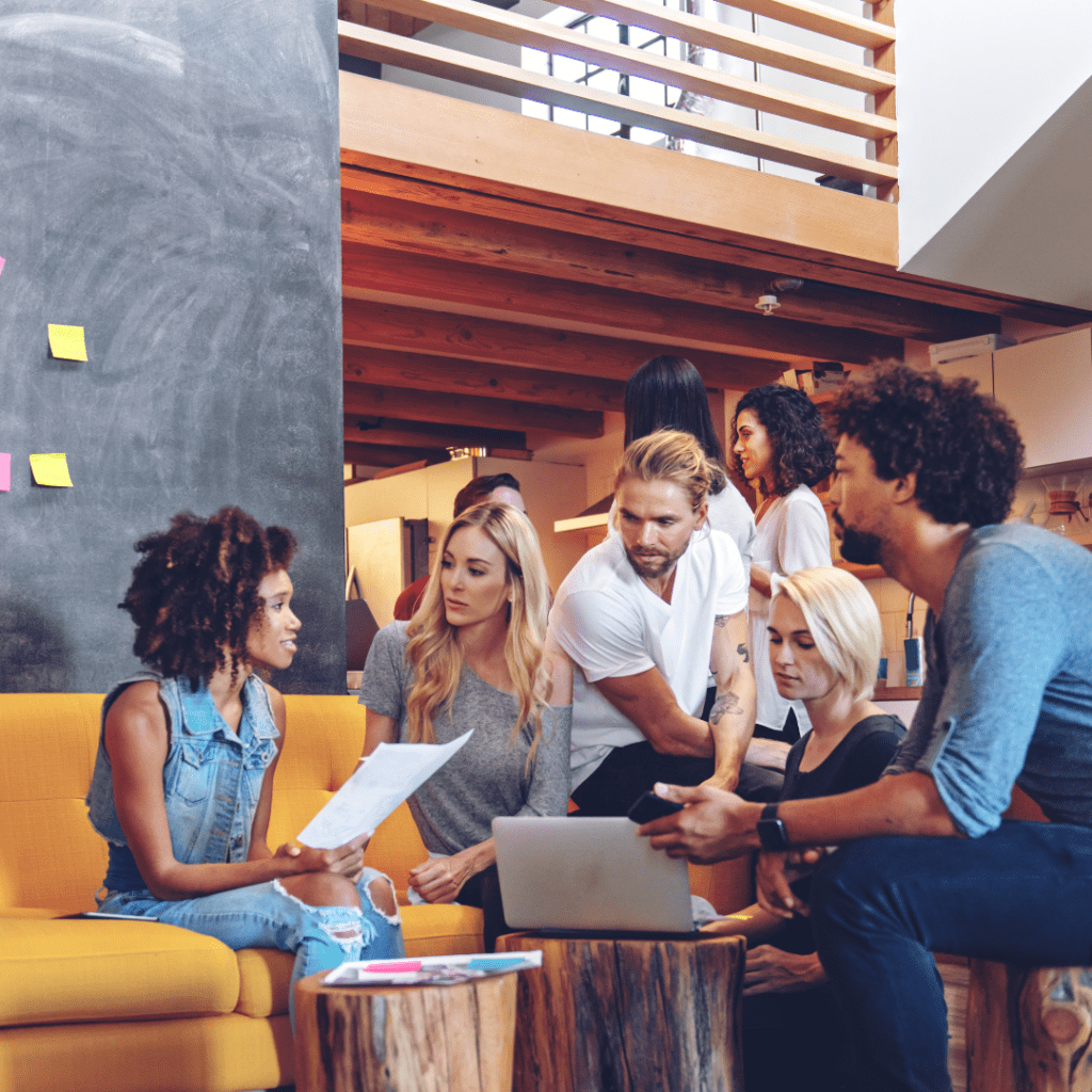 A diverse group of business professionals sits on a couch in an office, engaging in a brainstorming session.